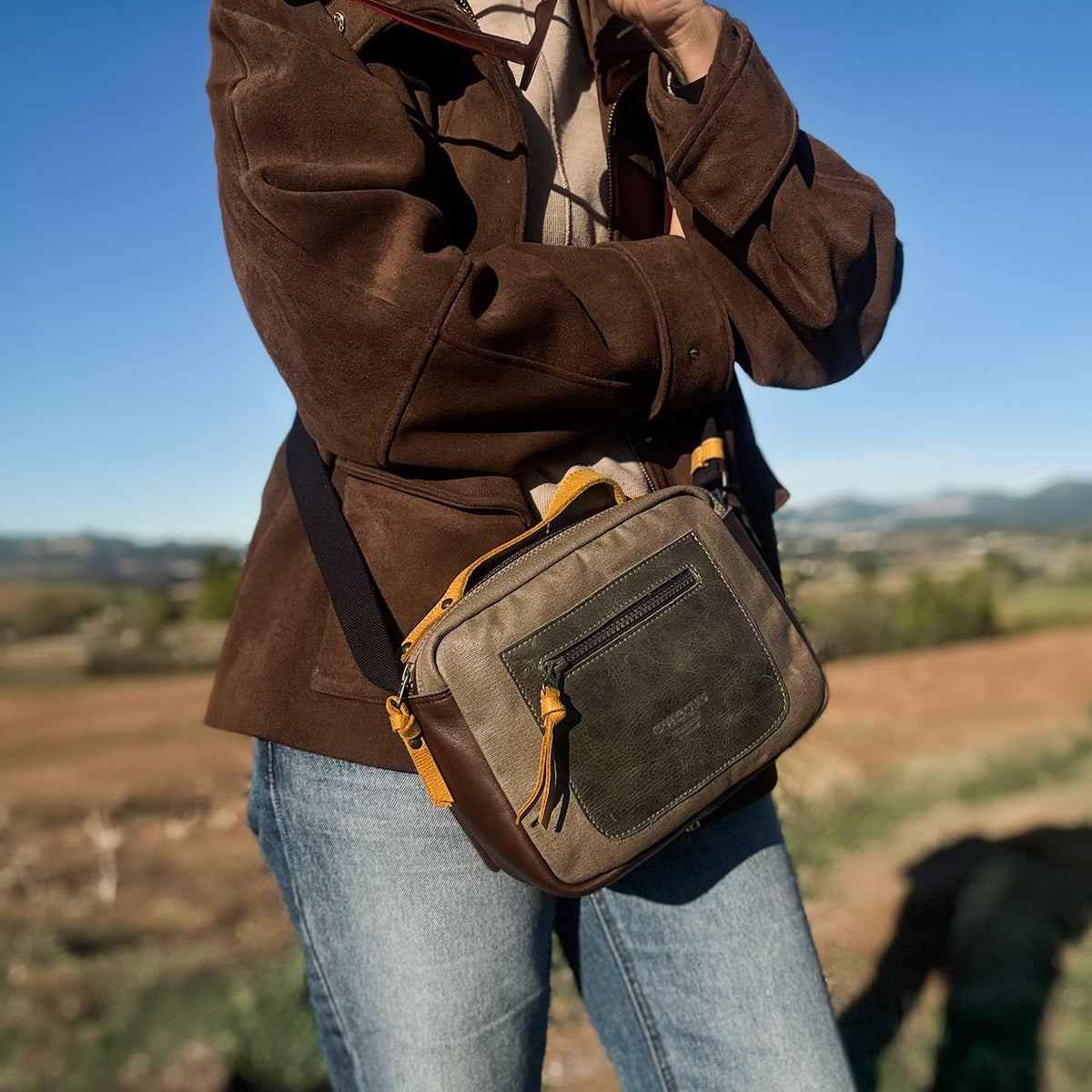 Mujer con chaqueta marrón y la bandolera Trend taupe de lona y piel, en el campo