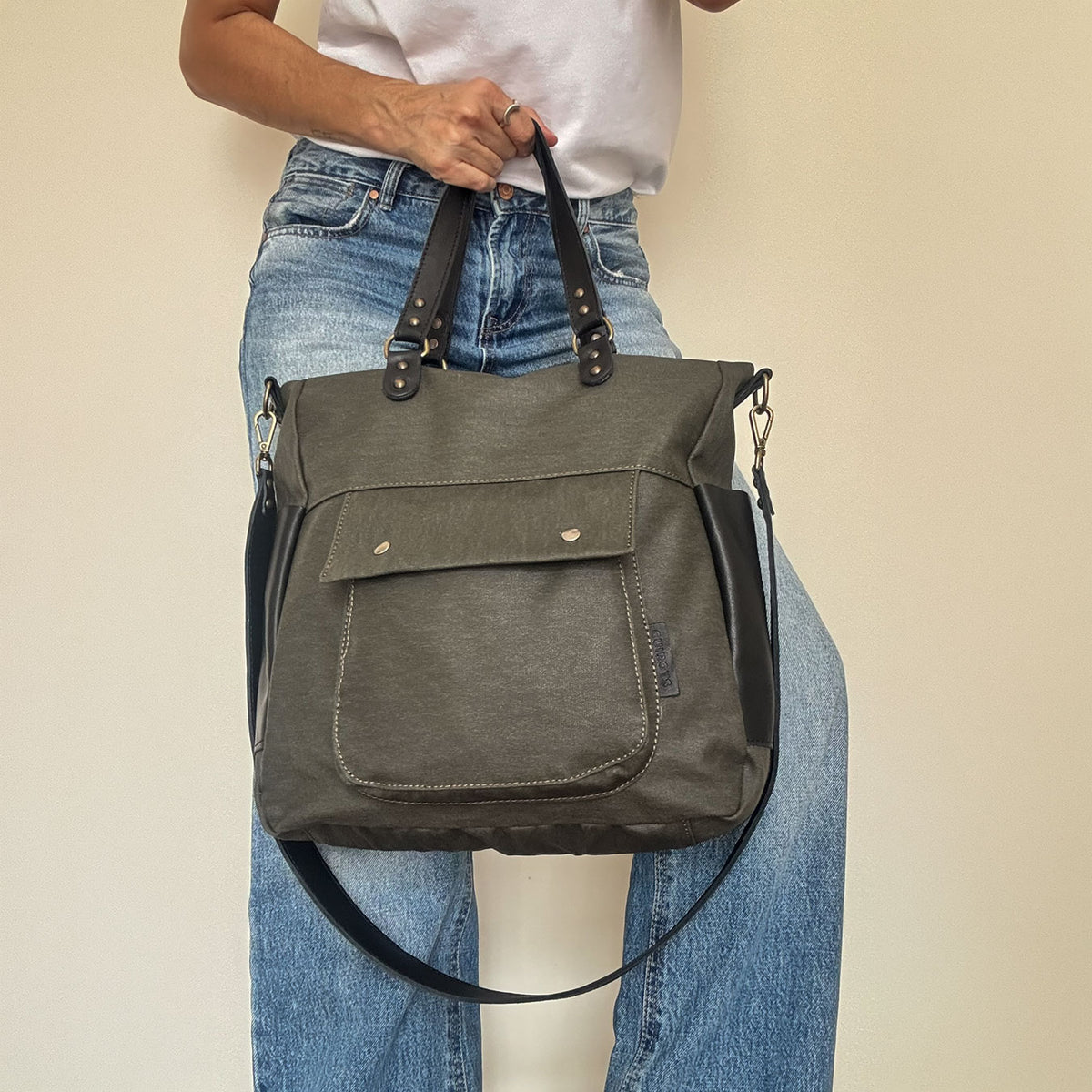 Bolso de mano y bandolera Barbour en color kaki, llevado de la mano