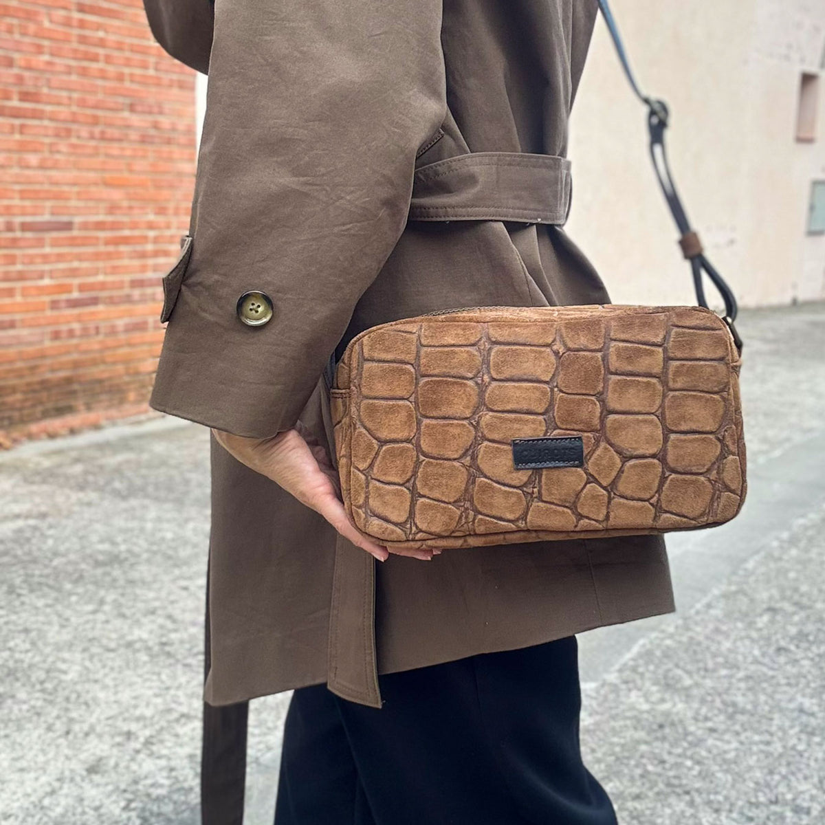 Bolso bandolera Coco de serraje con grabado tipo coco en color camel, llevado cruzado sobre una gabardina