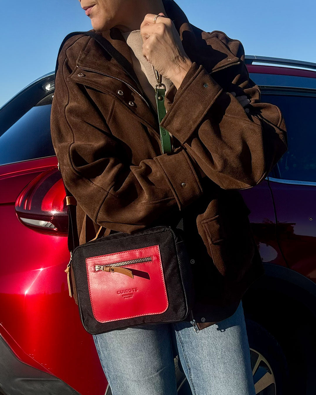 Mujer con la bandolera Trend negra con bolsillo de piel roja, junto a un coche rojo
