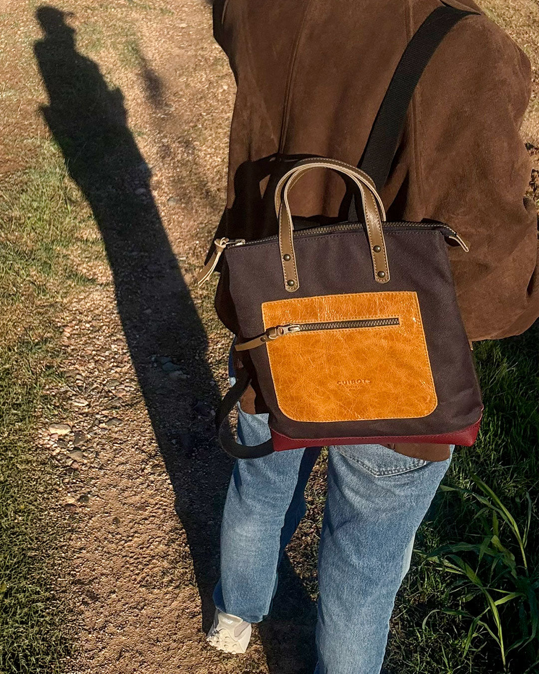 Mochila pequeña Trend marrón con bolsillo de piel camel, llevada a la espalda en un camino