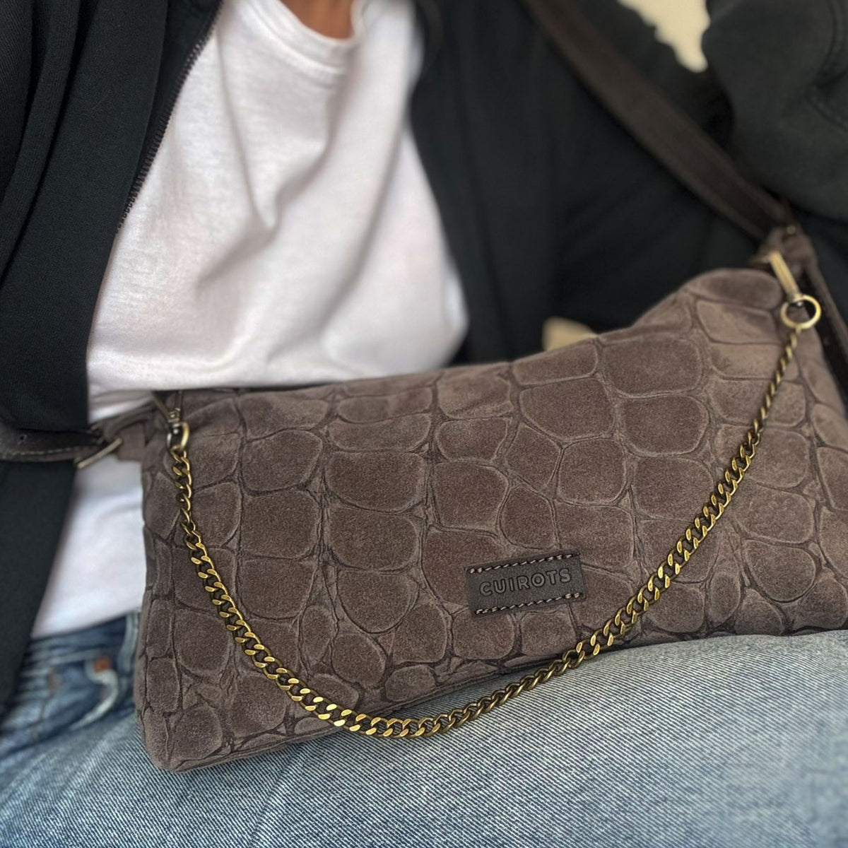 Bolso de hombro y bandolera Coco de serraje en color taupe, con asa de cadena, sobre unos vaqueros